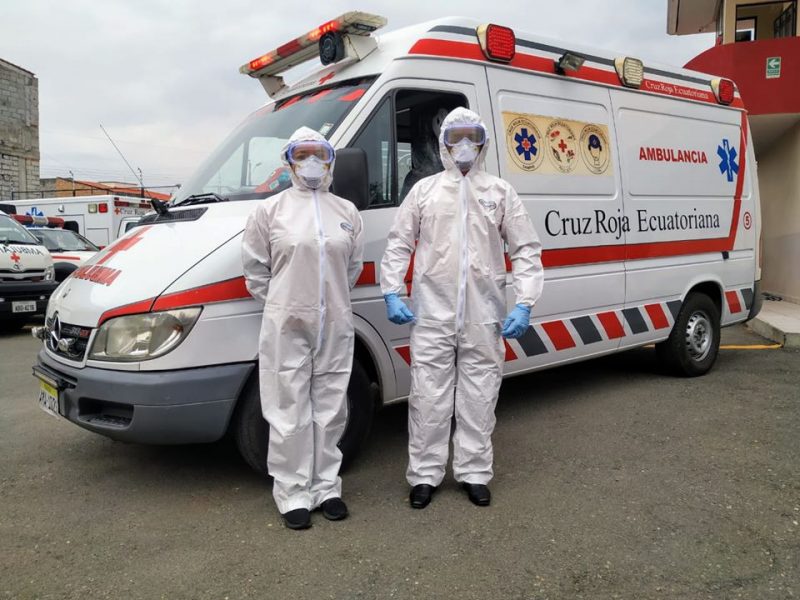 Deux employés de la Croix-Rouge équatorienne posent en équipement de protection individuelle devant un véhicule de l'organisation.