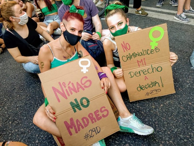 Deux jeunes filles, assisses par terre, tenant des pancartes contenant des slogans pro-avortement.