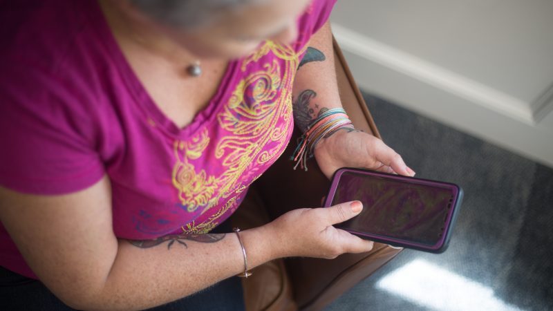 Une femme d'âge mûr au t-shirt coloré consulte son téléphone portable.