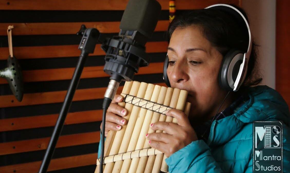 Une femme joue de la flute de pan devant un micro et avec un casque sur les oreilles dans un studio d'enregistrement